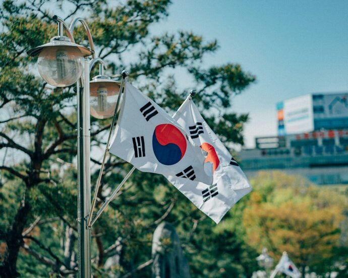 Two South Korean flags waving on a metal pole near pine trees
