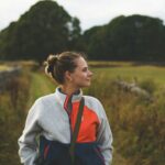 A woman with hair in a bun wearing a fleece jacket in a field