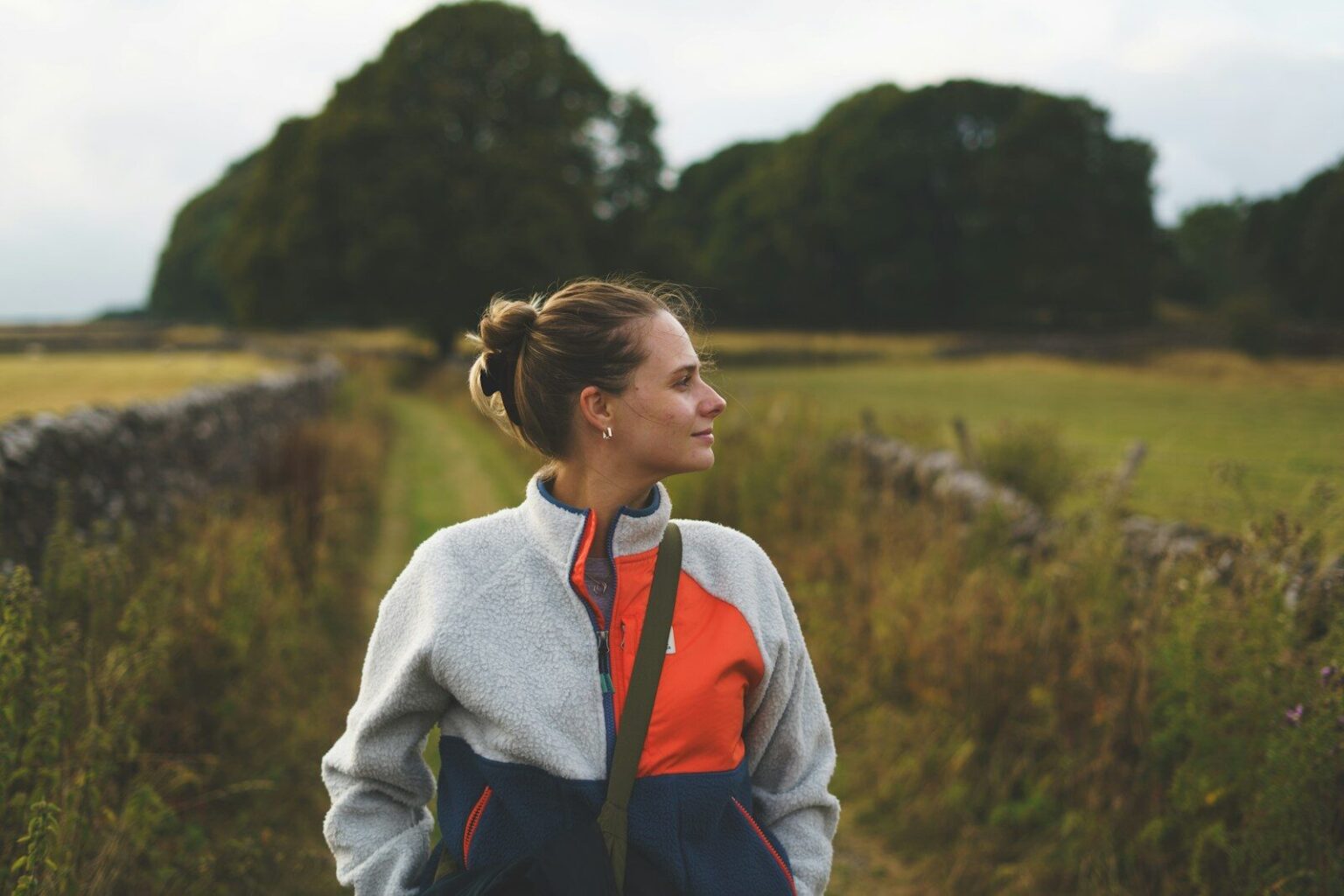 A woman with hair in a bun wearing a fleece jacket in a field