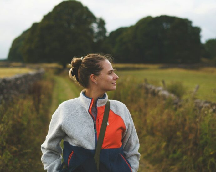 A woman with hair in a bun wearing a fleece jacket in a field